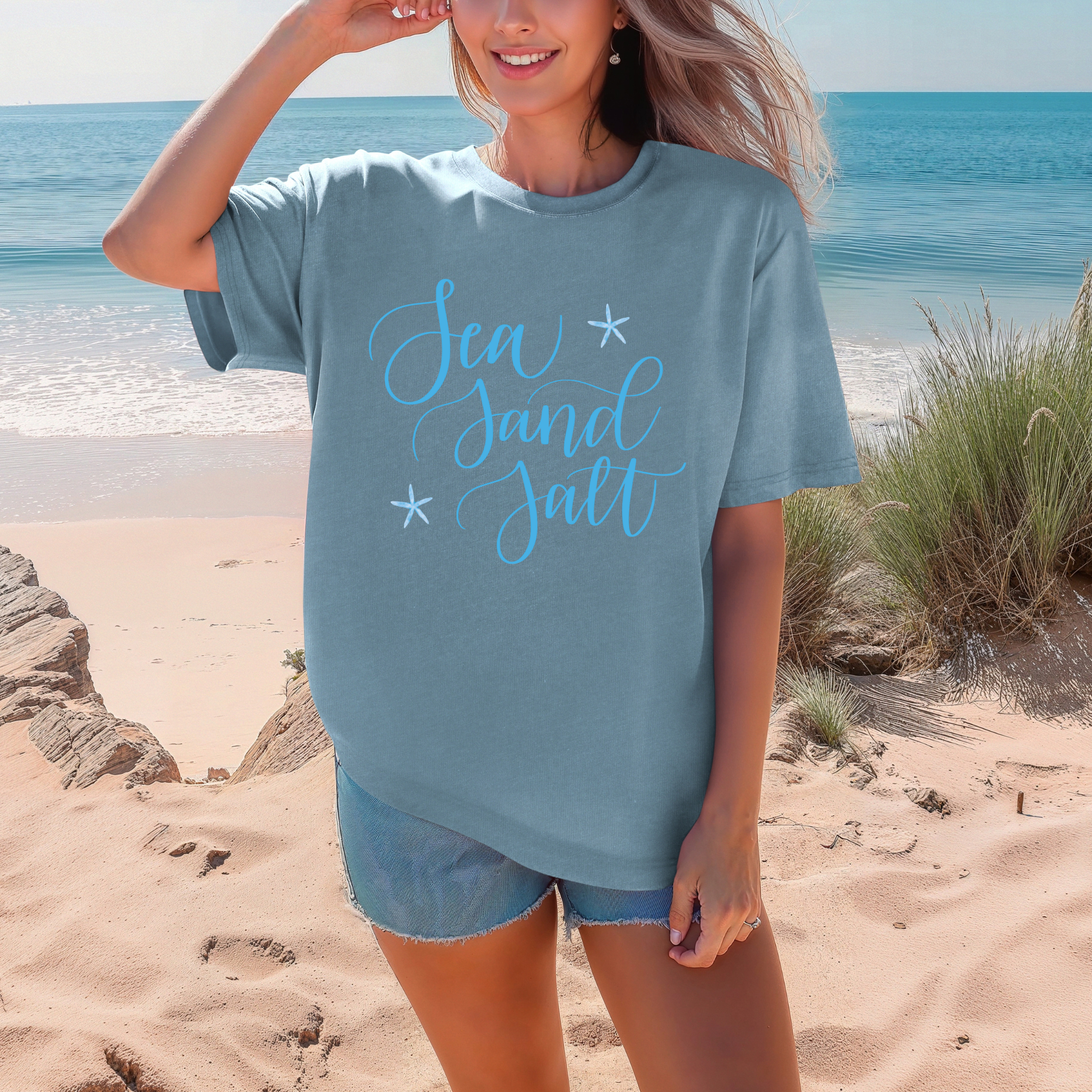 Woman wearing a blue t-shirt with 'Sea Sand Salt' text on a beach