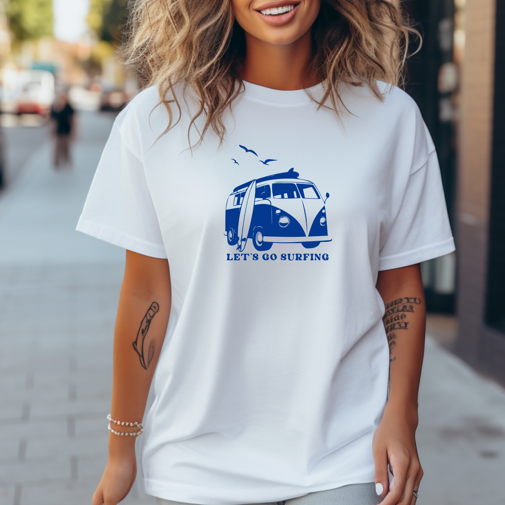 Person wearing a white t-shirt with a blue graphic and text, standing on a street.