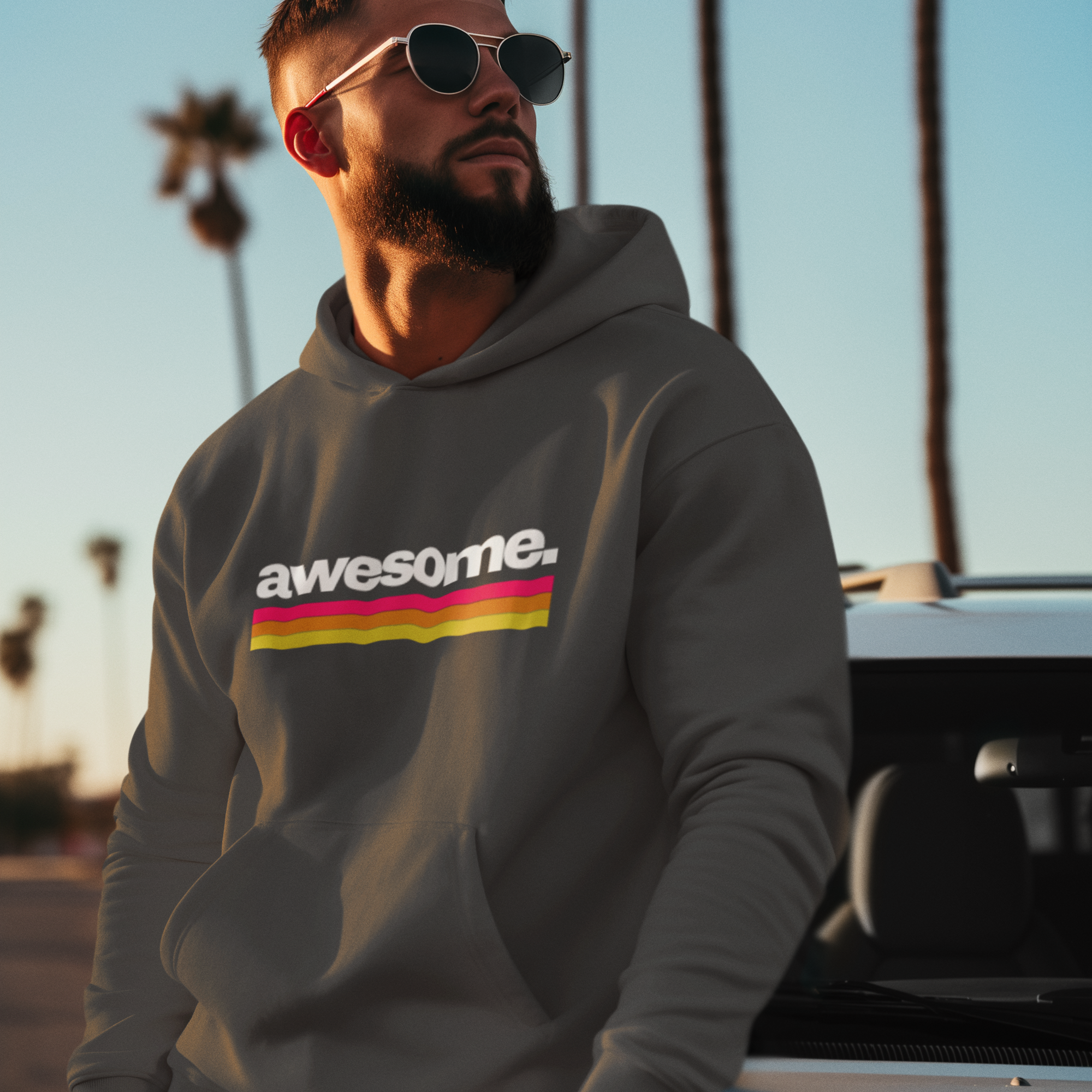 Man wearing a hoodie with 'awesome' printed on it, standing in front of palm trees.