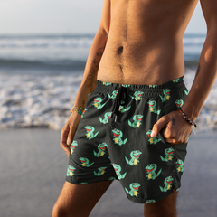 Man wearing black swim shorts with green alligator pattern on a beach.
