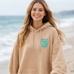 Woman wearing a beige hoodie with a beach graphic palm trees and hibiscus flowers
