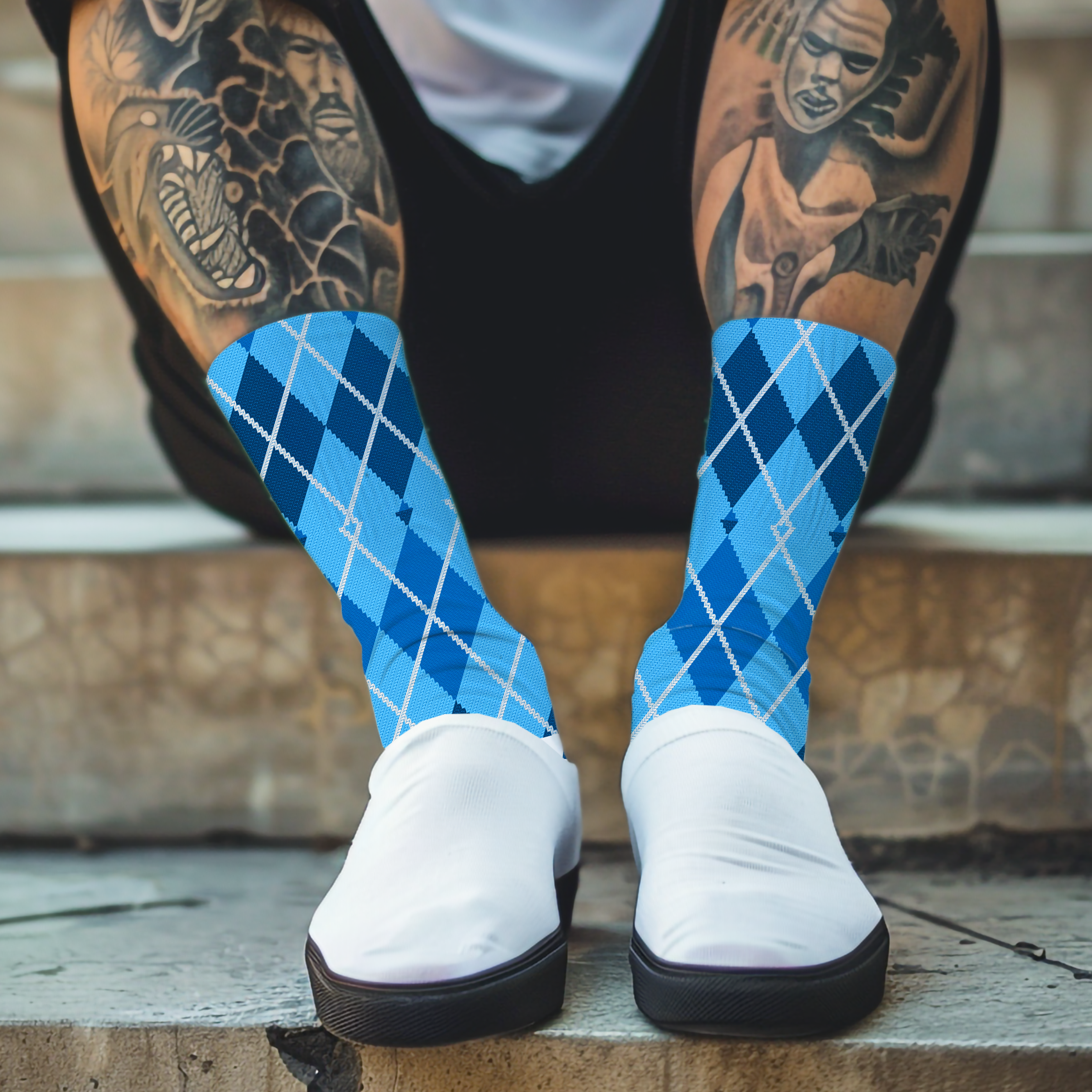 Person wearing blue argyle socks and white sneakers with tattoos on their legs, sitting on steps.
