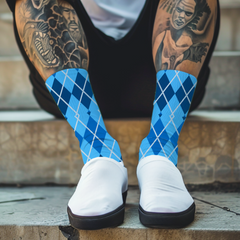 Person wearing blue argyle socks and white sneakers with tattoos on their legs, sitting on steps.