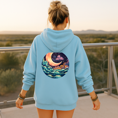 Person wearing a light blue hoodie with a celestial design on the back, standing on a balcony with a scenic view.