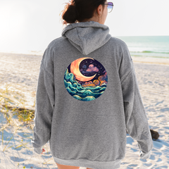 Person wearing a gray hoodie with a celestial design on the beach