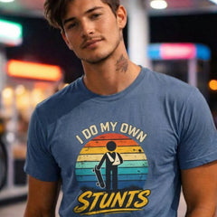 Man wearing a blue t-shirt with 'I Do My Own Stunts' graphic design in a neon-lit urban setting.