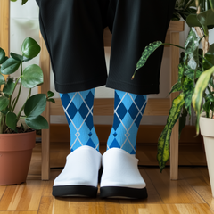 Person wearing blue argyle socks with white shoes in a room with plants.