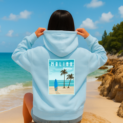 Person wearing a light blue hoodie with a Malibu design on a beach