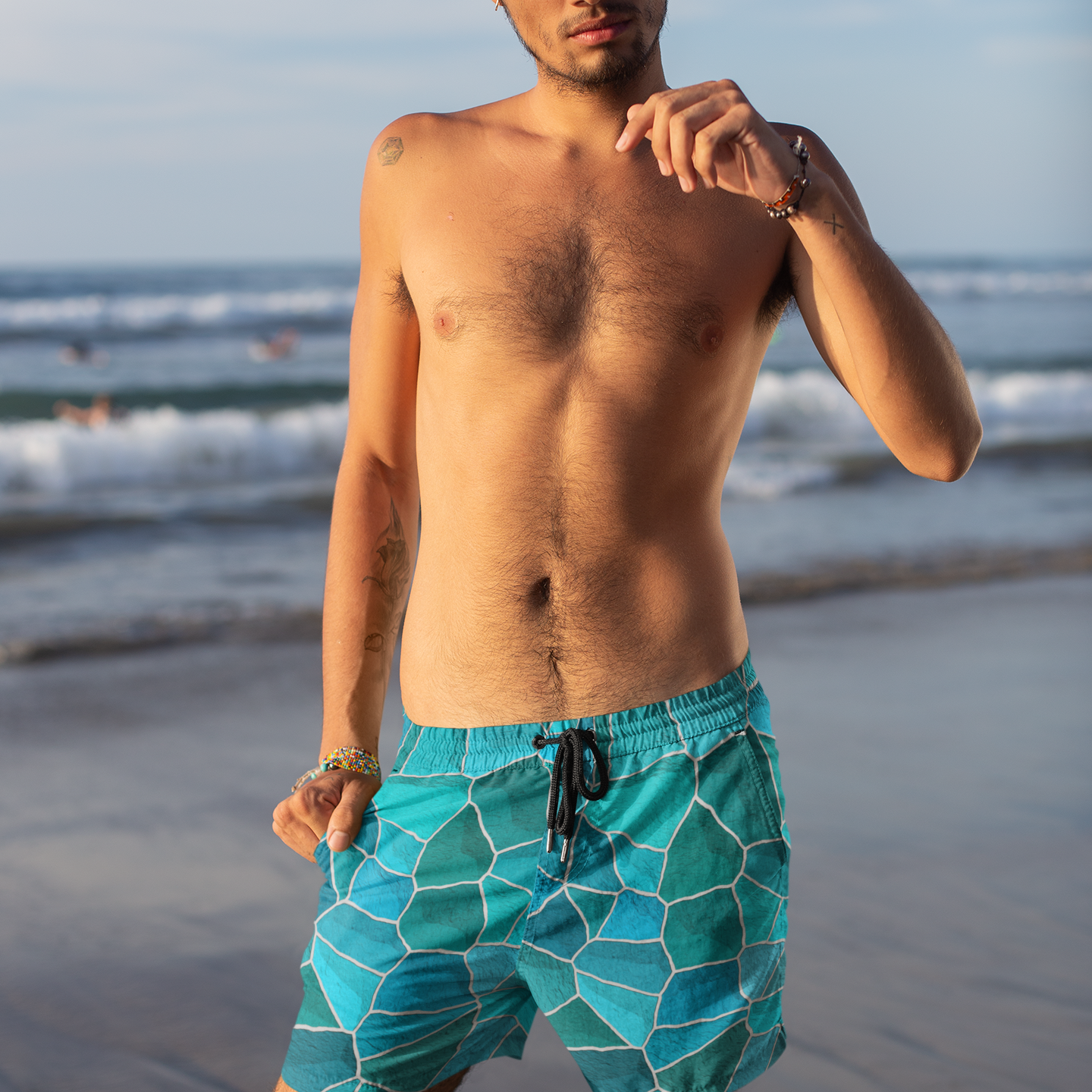 Man wearing teal swim shorts with a geometric pattern on a beach.