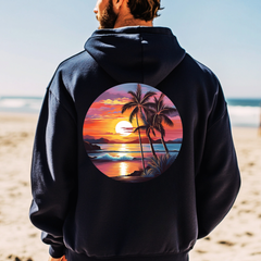 Person wearing a black hoodie with a tropical sunset design on a beach