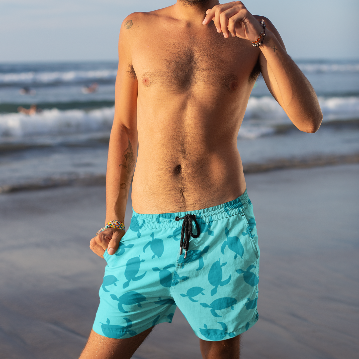 Man wearing turquoise swim shorts with a turtle pattern on a beach.