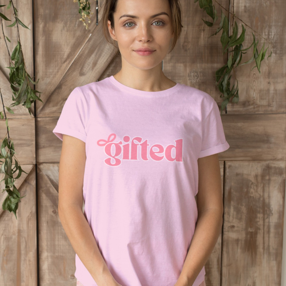 Woman wearing a pink t-shirt with 'gifted' text against a wooden background