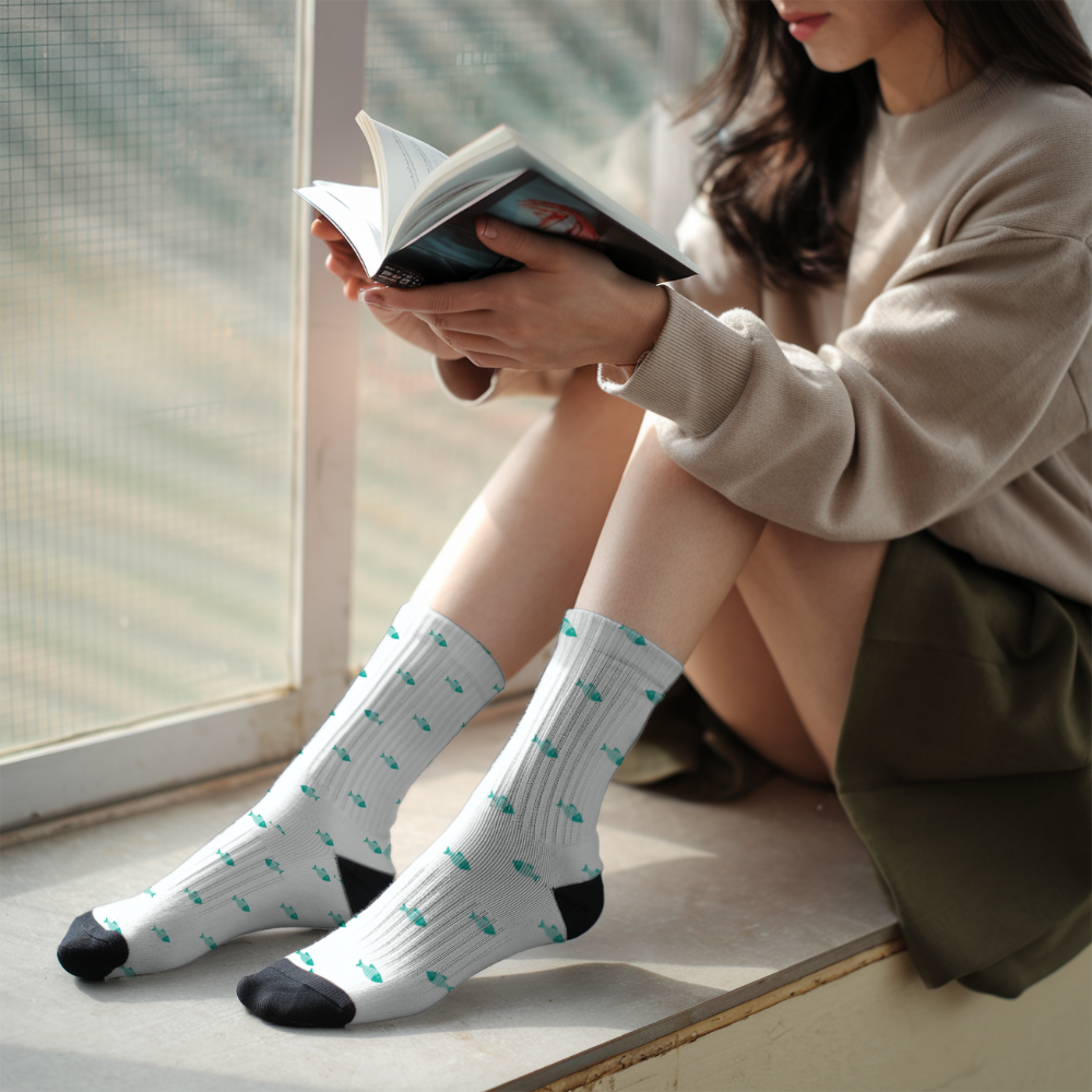 Person wearing white socks with black toes and green patterns, sitting by a window reading a book.