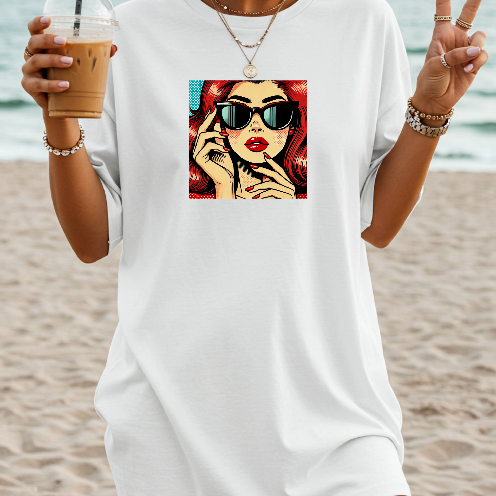 Person wearing a white t-shirt with a graphic design of a woman with sunglasses and red hair, holding a drink on a beach.