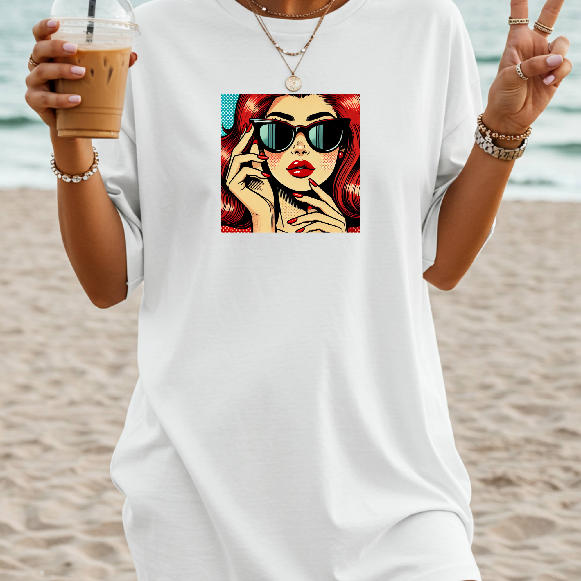 Person wearing a white t-shirt with a graphic design of a woman with sunglasses and red hair, holding a drink on a beach.