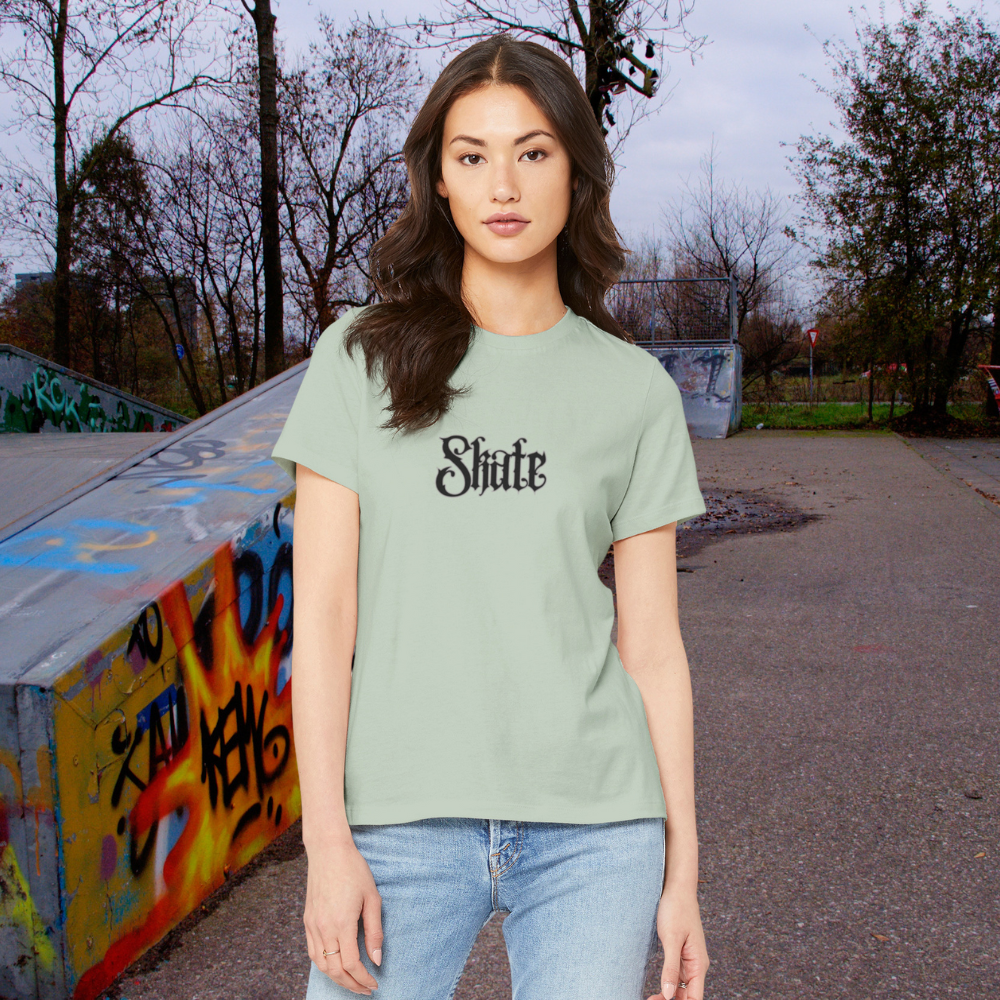 Woman wearing a light green t-shirt with 'Shite' printed on it, standing in an urban setting with graffiti.