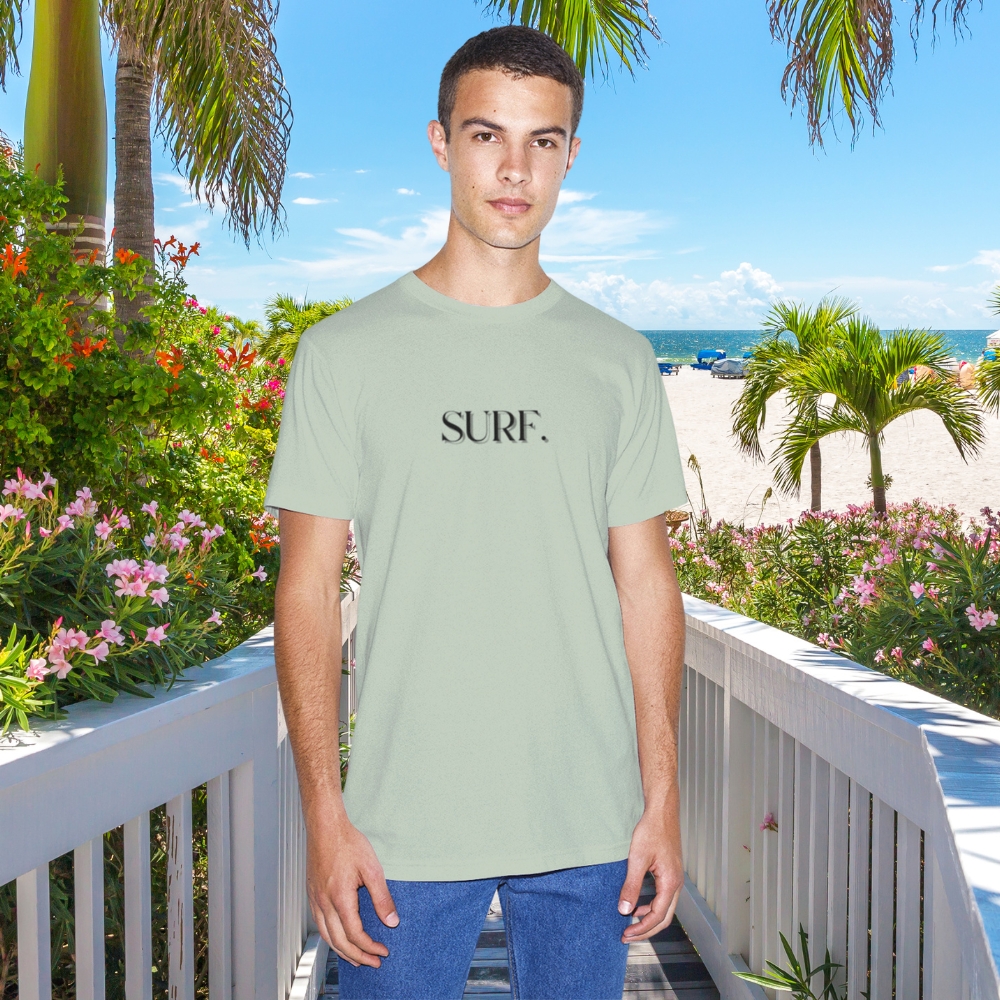 Man wearing a light green t-shirt with 'SURF.' text, standing on a balcony with a beach view.