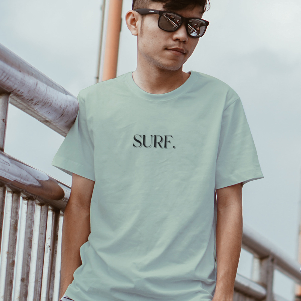 Person wearing a light green t-shirt with 'SURF.' text, standing outdoors.