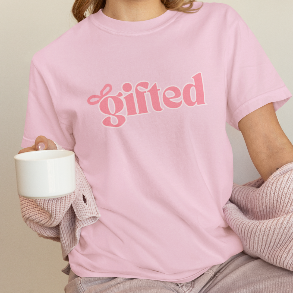Person wearing a pink t-shirt with 'gifted' text, holding a white mug.
