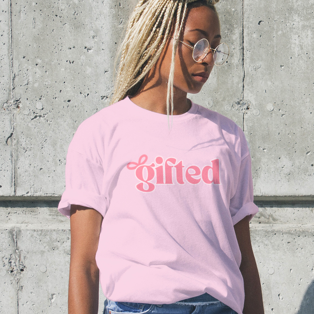 Person wearing a pink t-shirt with 'gifted' text against a concrete wall.