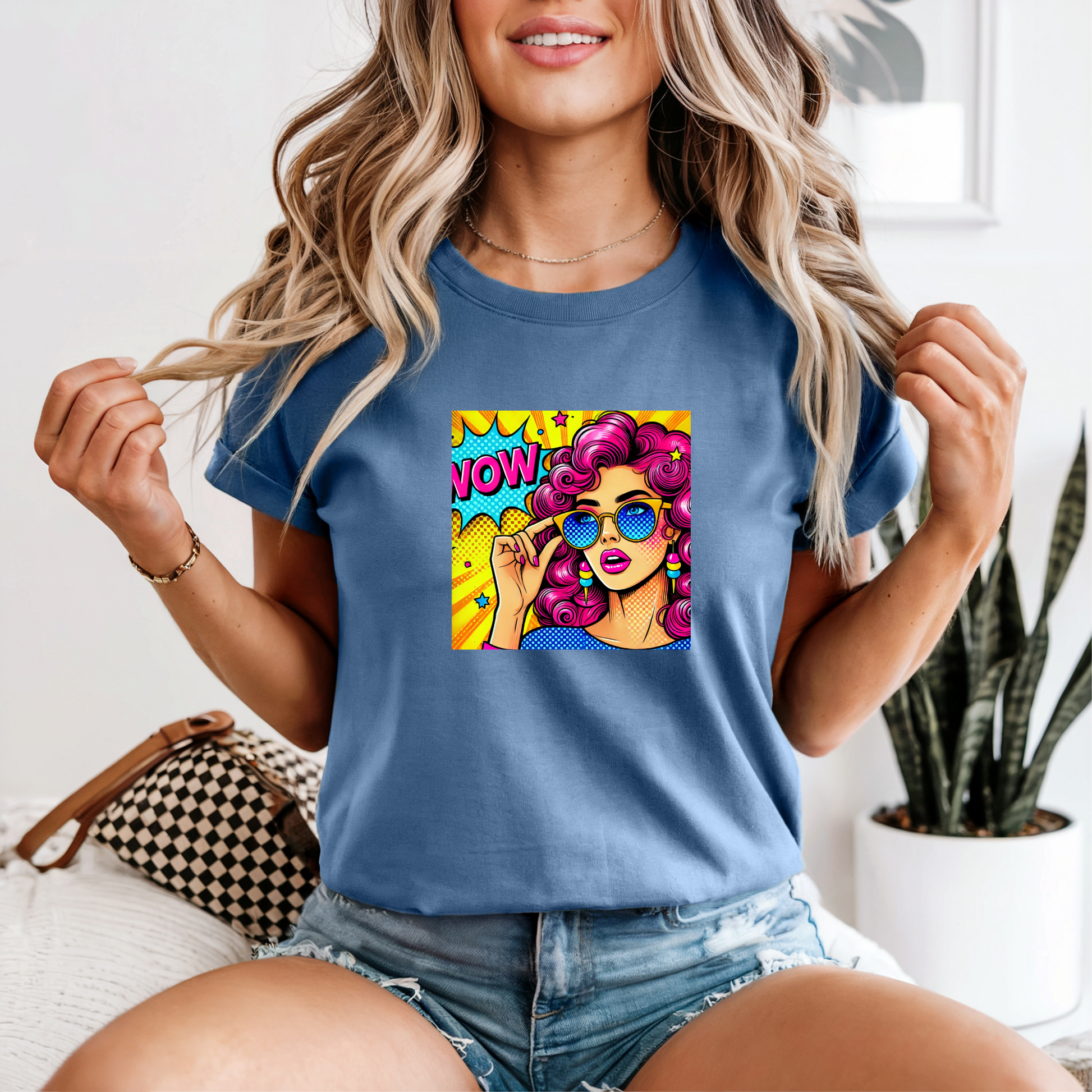 Woman wearing a blue t-shirt with a colorful graphic design of a woman with pink hair and sunglasses.