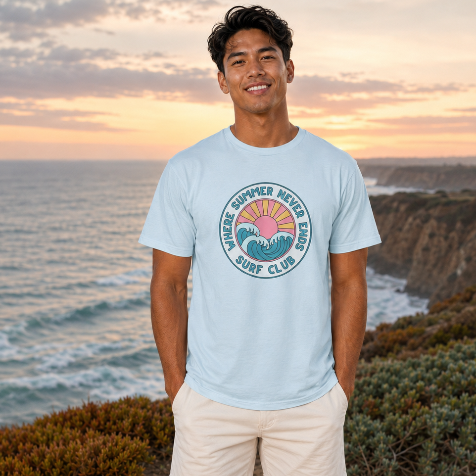 A man standing on a coastal cliff path at sunset wearing a light blue graphic t-shirt and cream shorts. The t-shirt features a circular graphic that reads 'MORIRI SUMMER BEACH CLUB SURF CLUB' with a sunset and wave design.