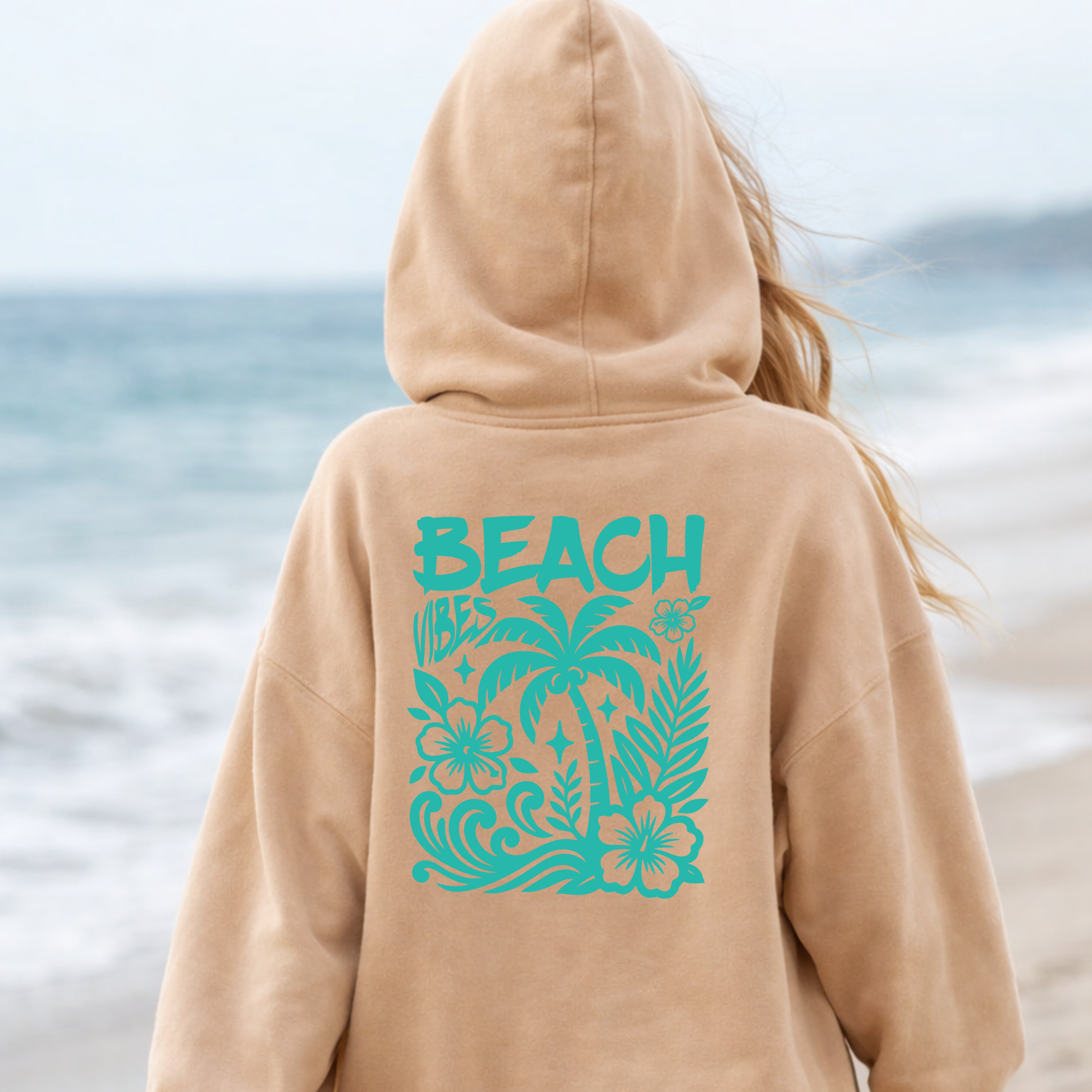 Person wearing a beige hoodie with 'BEACH' and palm tree design on a beach