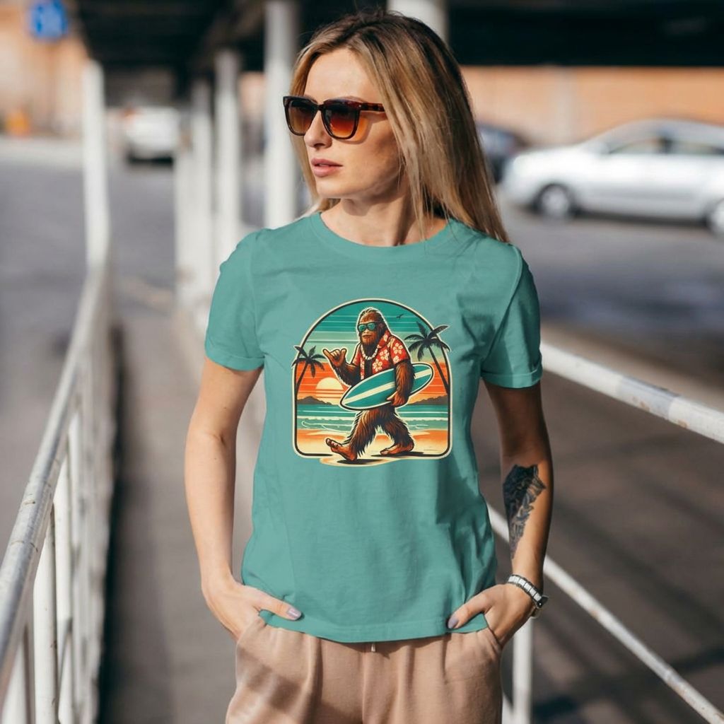 Woman wearing a teal t-shirt with a graphic design of a bigfoot holding a surfboard on a city street.