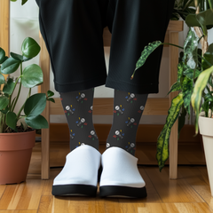 Person wearing black microphone socks with colorful patterns and white shoes in a room with plants.