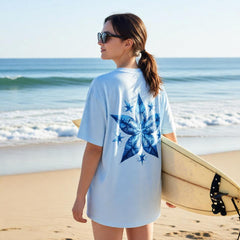 Woman on a beach holding a surfboard wearing a light blue t-shirt with a blue starfish design.