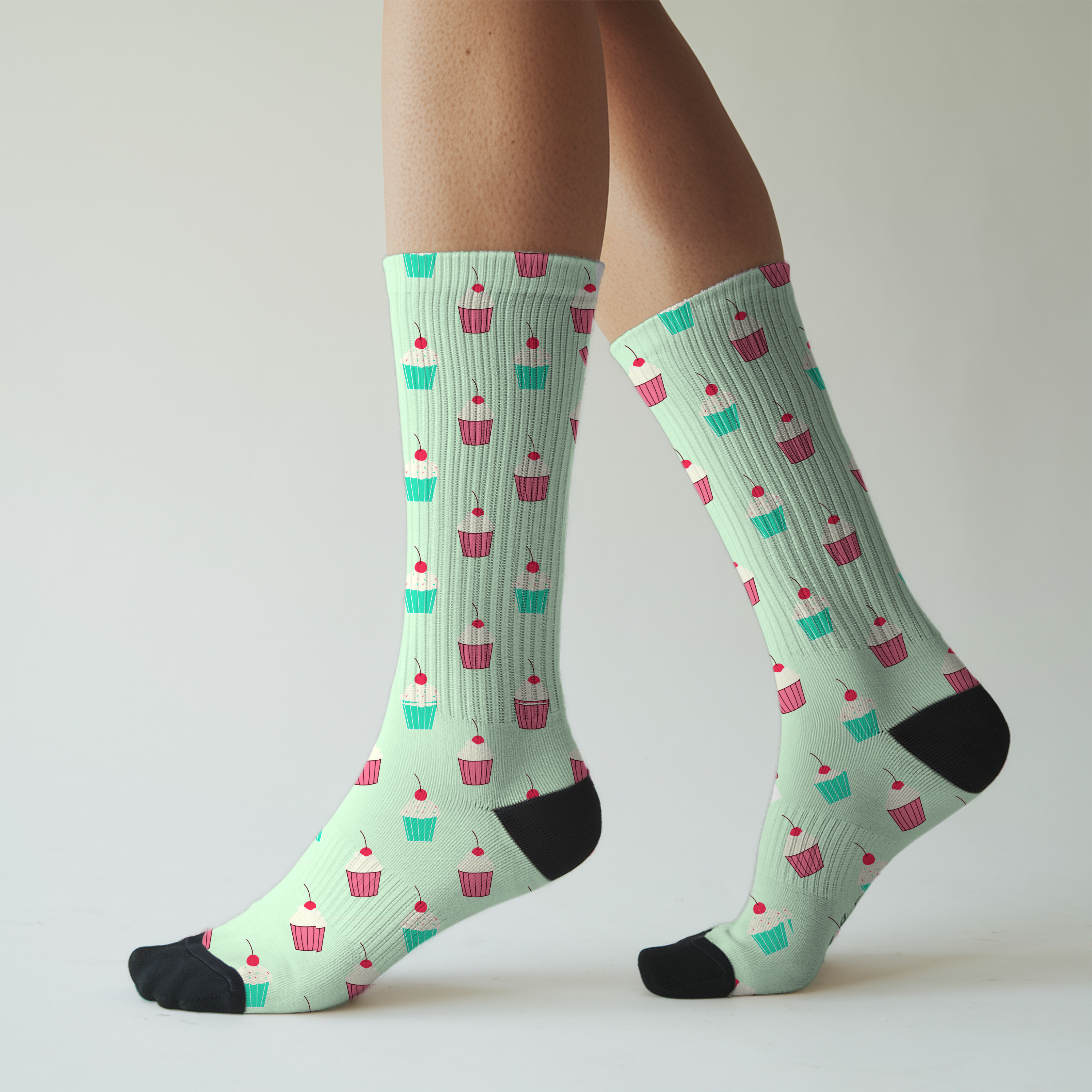 Mint green socks with cupcake pattern worn by a person on a light gray background