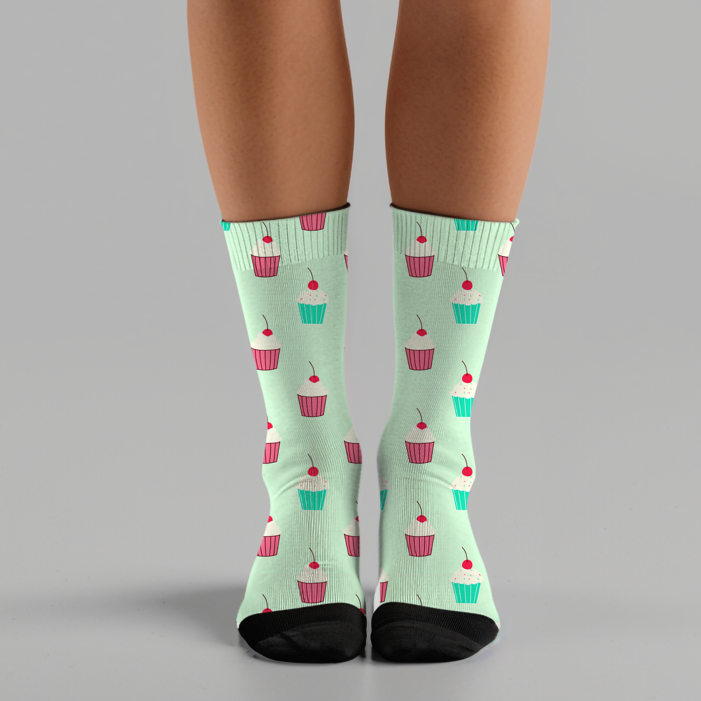 Light green socks with cupcake pattern worn by a person on a gray background