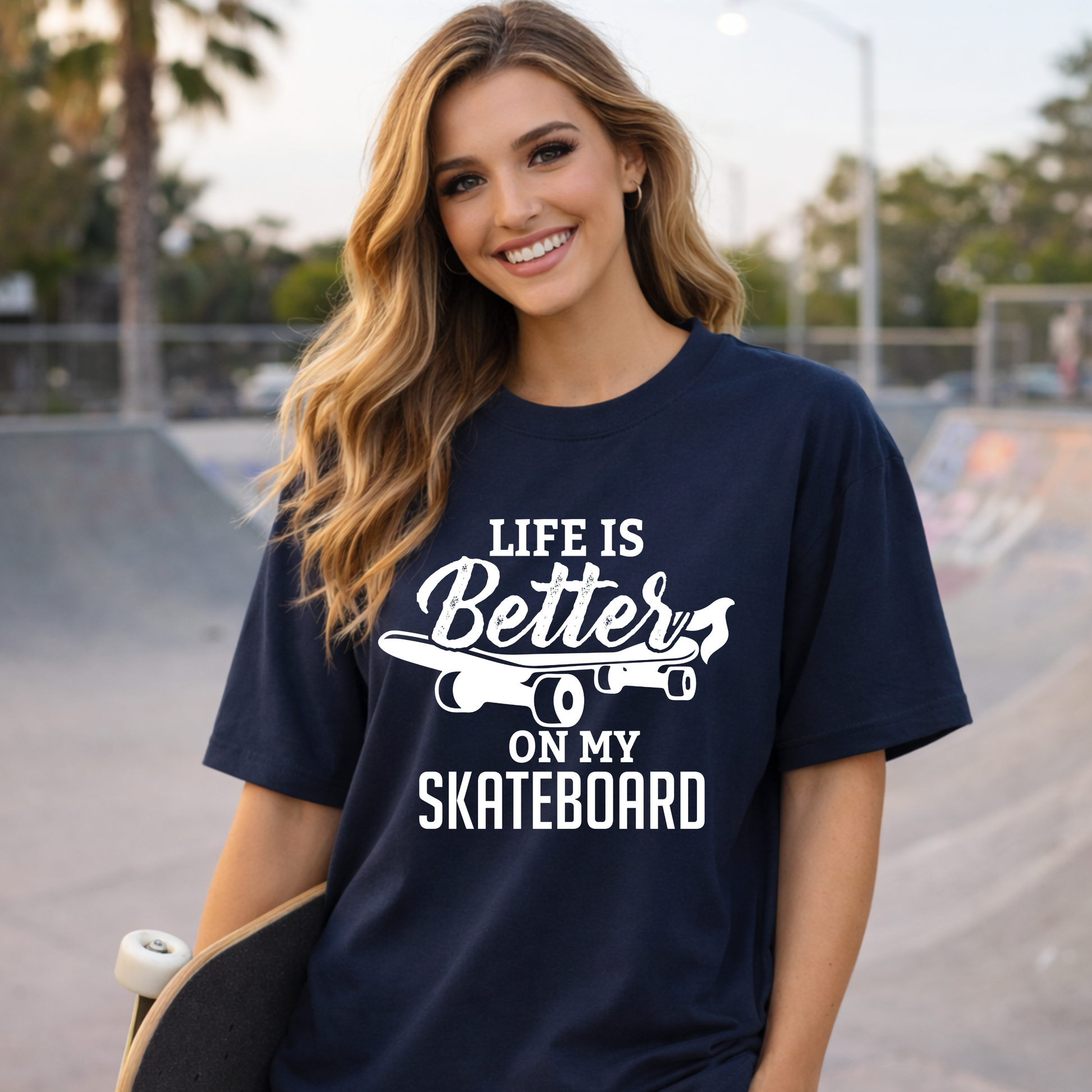 Woman wearing a navy blue t-shirt with 'Life is Better on my Skateboard' text at a skate park.