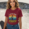 Woman wearing a maroon t-shirt with a graphic design and text, standing in front of a graffiti-covered wall.
