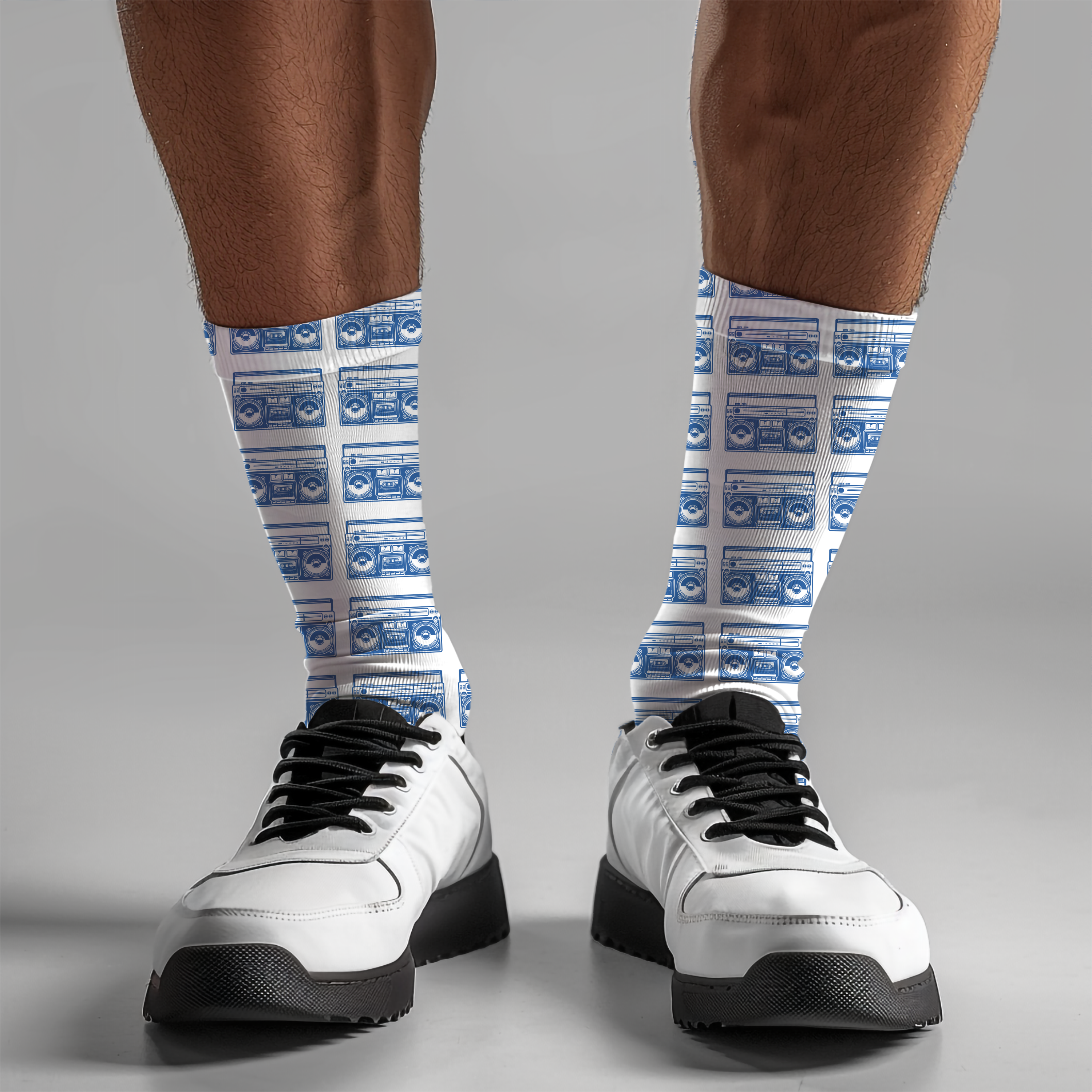 White sneakers with black laces worn on feet wearing socks with blue boom box pattern against a white background