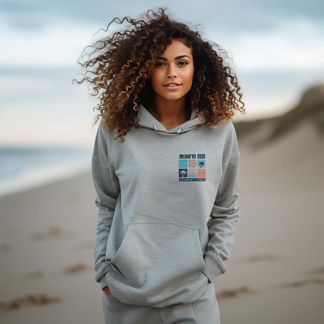 Person wearing a gray hoodie with 'Let's Go Surfing' text on a beach