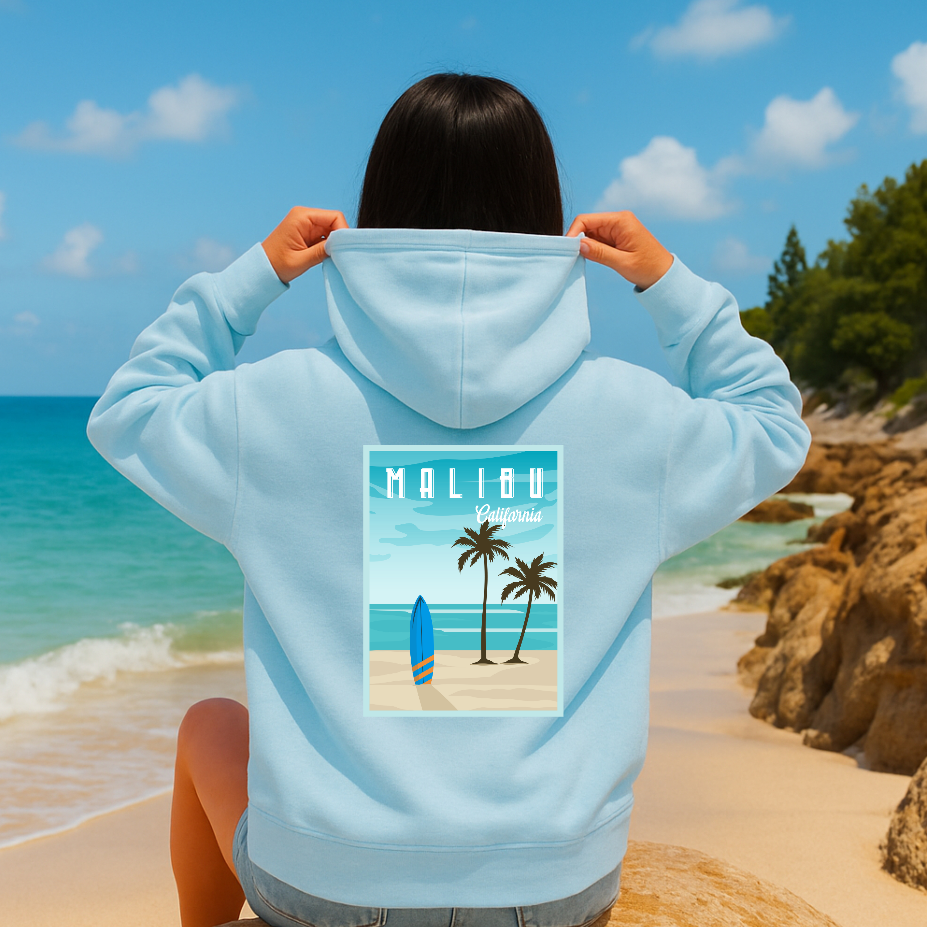 Person wearing a light blue hoodie with a Malibu design on a beach