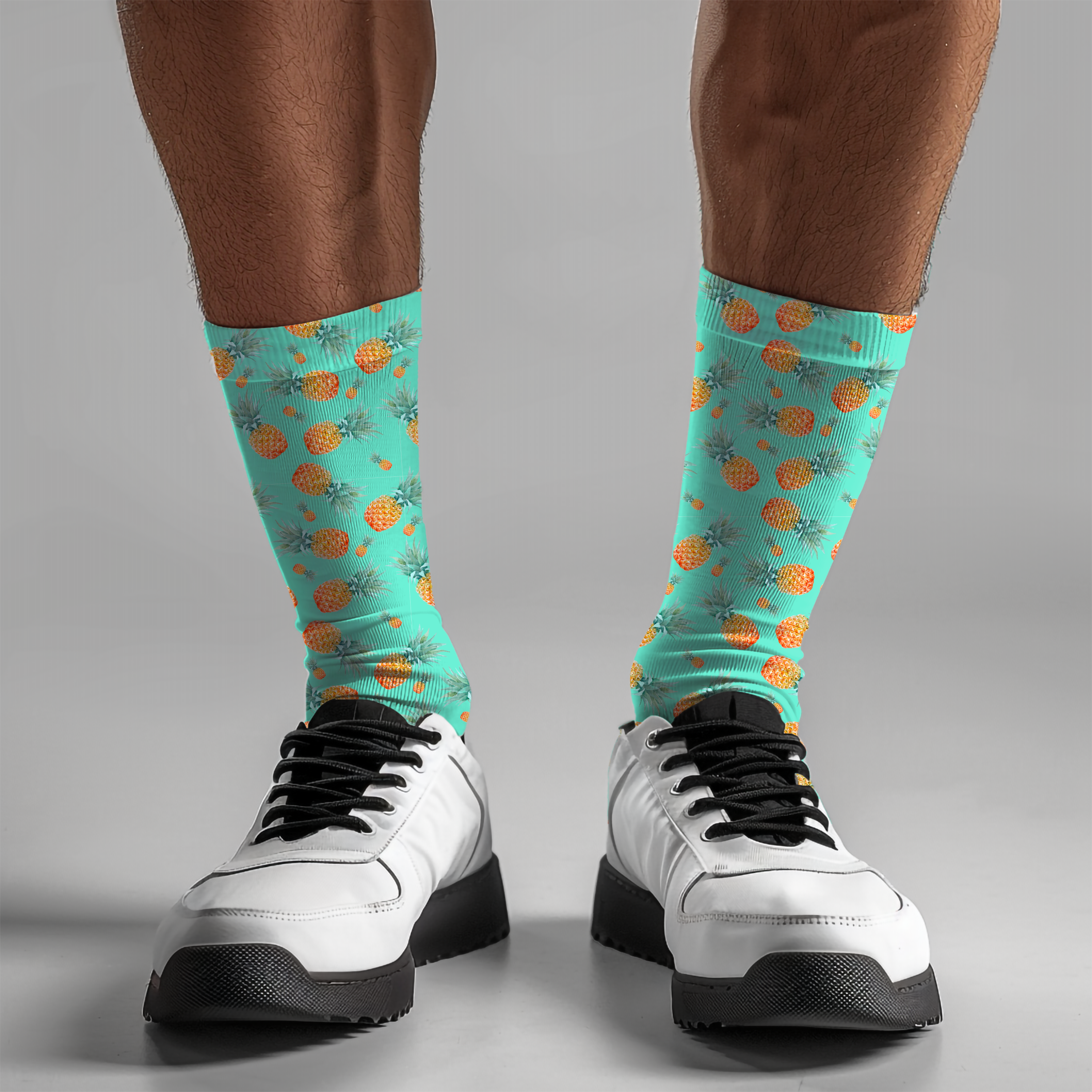 Teal socks with pineapple pattern worn with white sneakers on a gray background