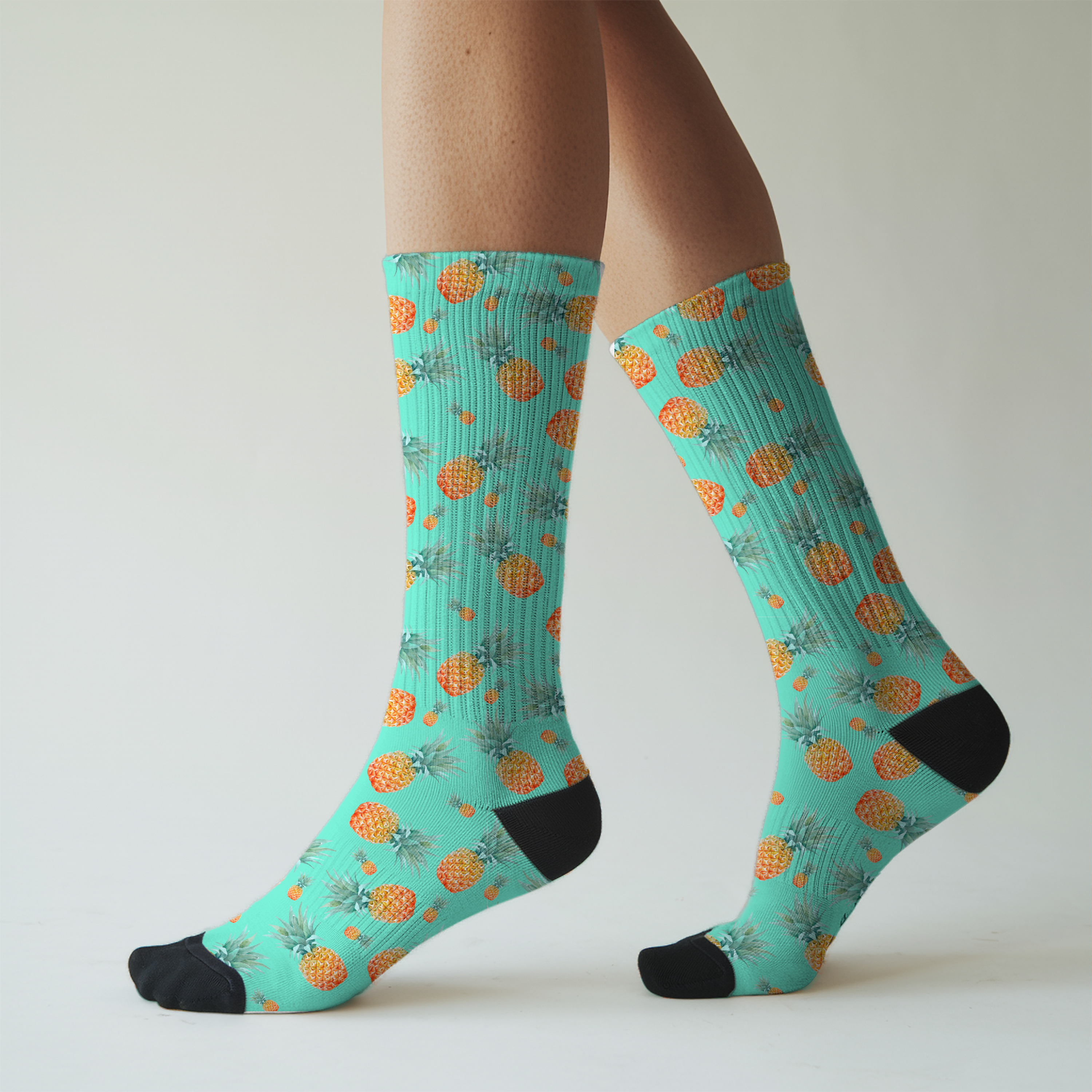 Teal socks with pineapple pattern worn by a person on a light gray background