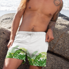 Man wearing white swim shorts with green leaf pattern on a beach.