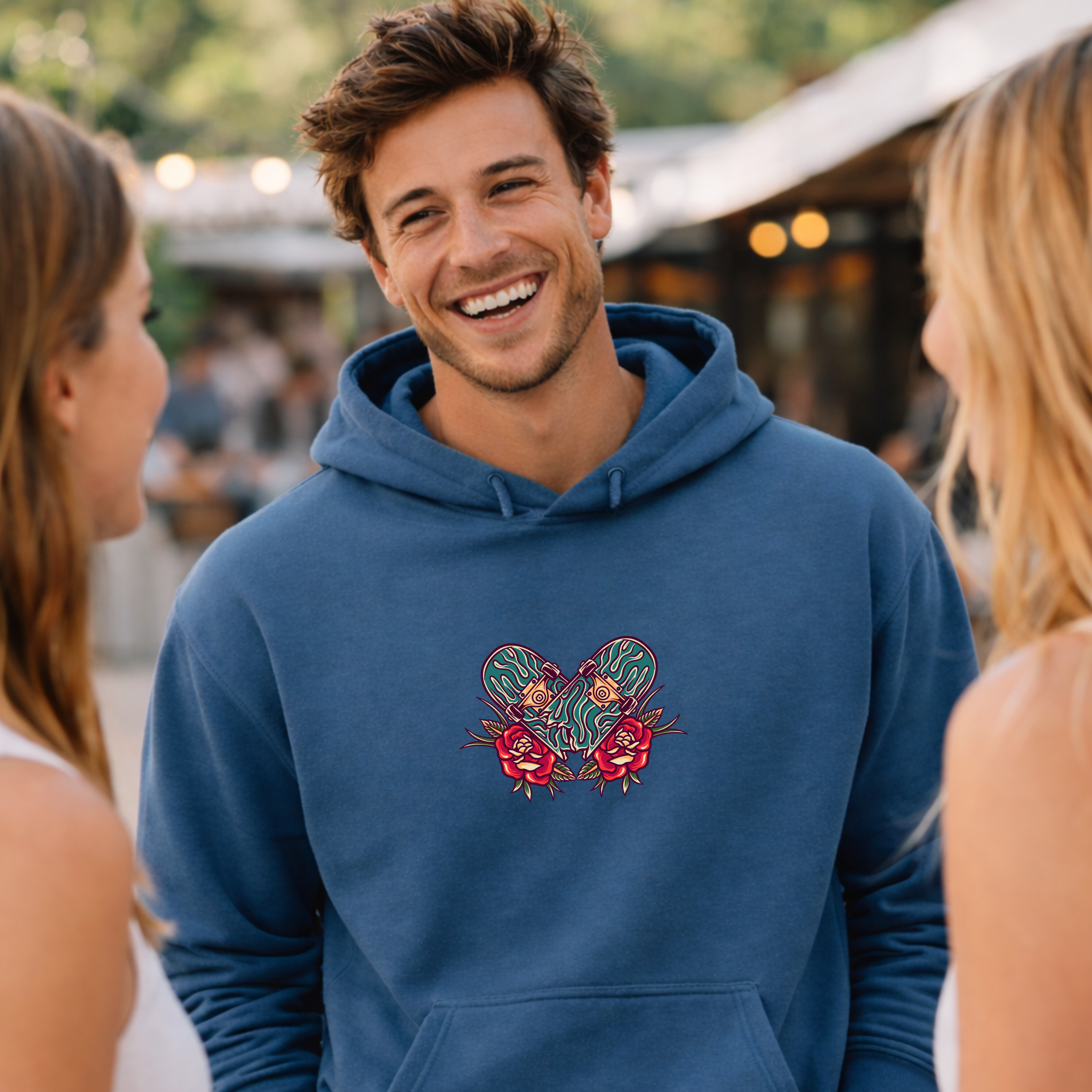 Man wearing a blue hoodie with a skateboard floral design, smiling and talking to two women outdoors.