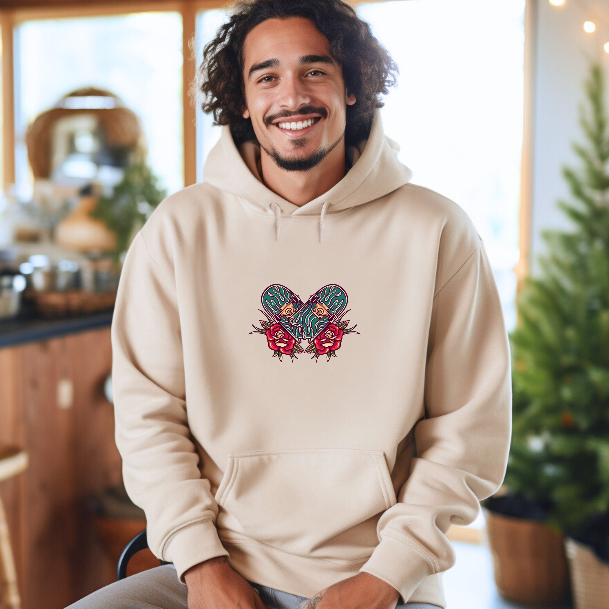 Man wearing a beige hoodie with a skateboard graphic, sitting in a kitchen.