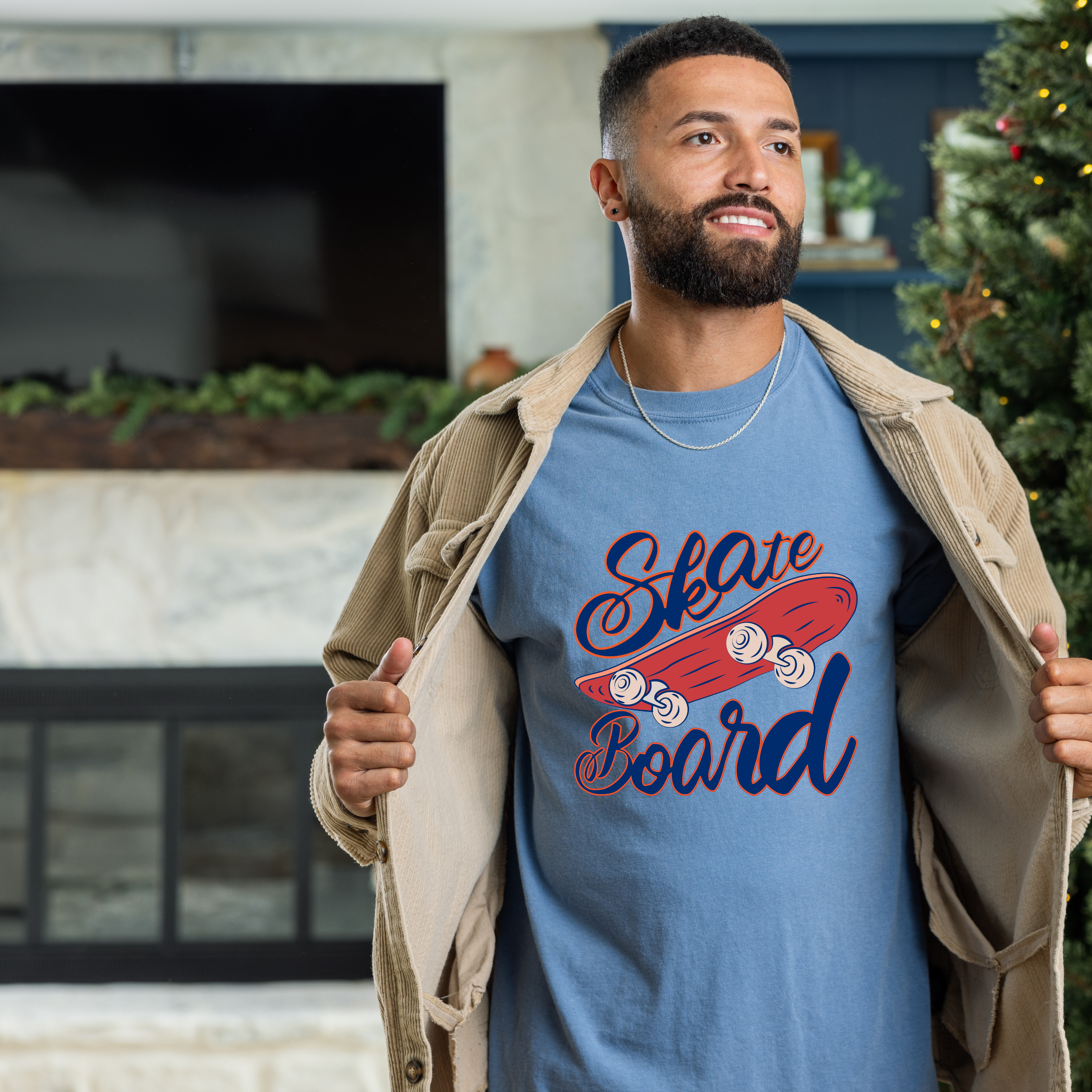 Man wearing a blue t-shirt with a skateboard graphic and text, standing in a room with a Christmas tree.
