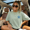 Woman sitting in a car wearing a bay green t-shirt with a blue starfish design.