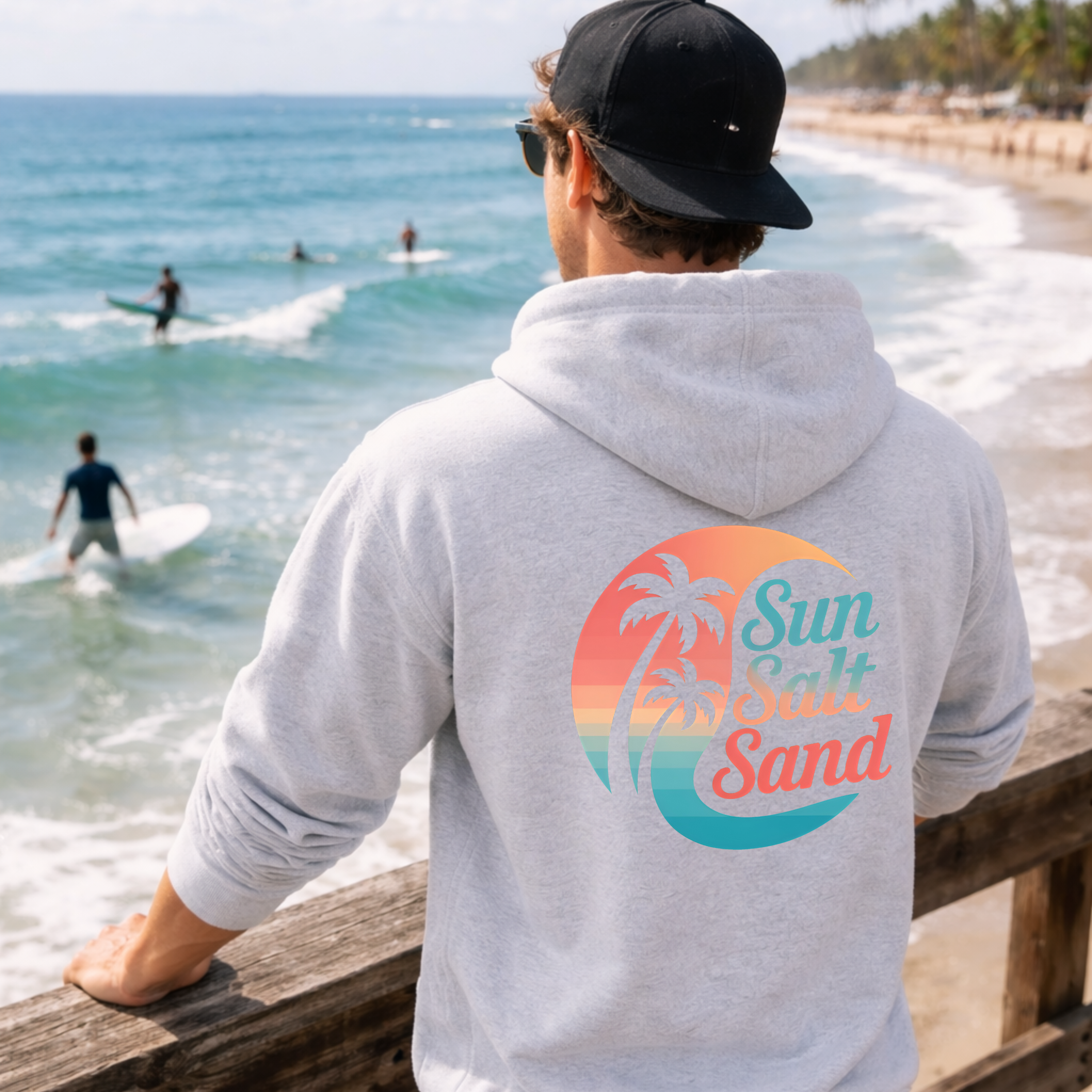 Person wearing a hoodie with 'Sun, Salt, Sand' design at the beach