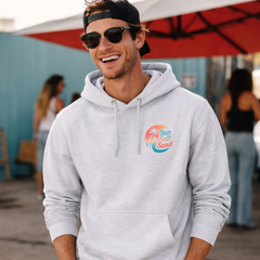 Man wearing a gray hoodie with a logo, smiling outdoors.