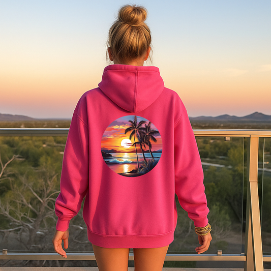 Person wearing a pink hoodie with a palm tree and sunset design, standing on a balcony with a scenic view.