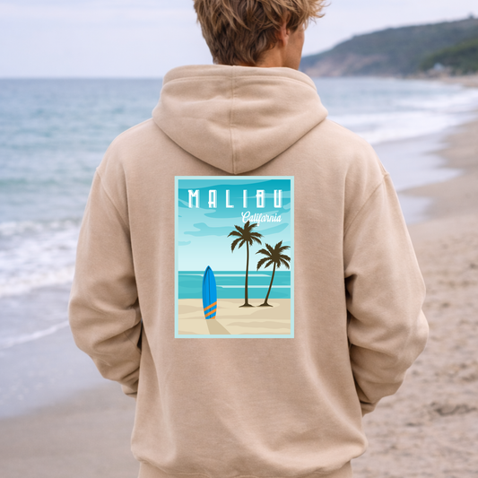 Person wearing a beige hoodie with a Malibu design on a beach