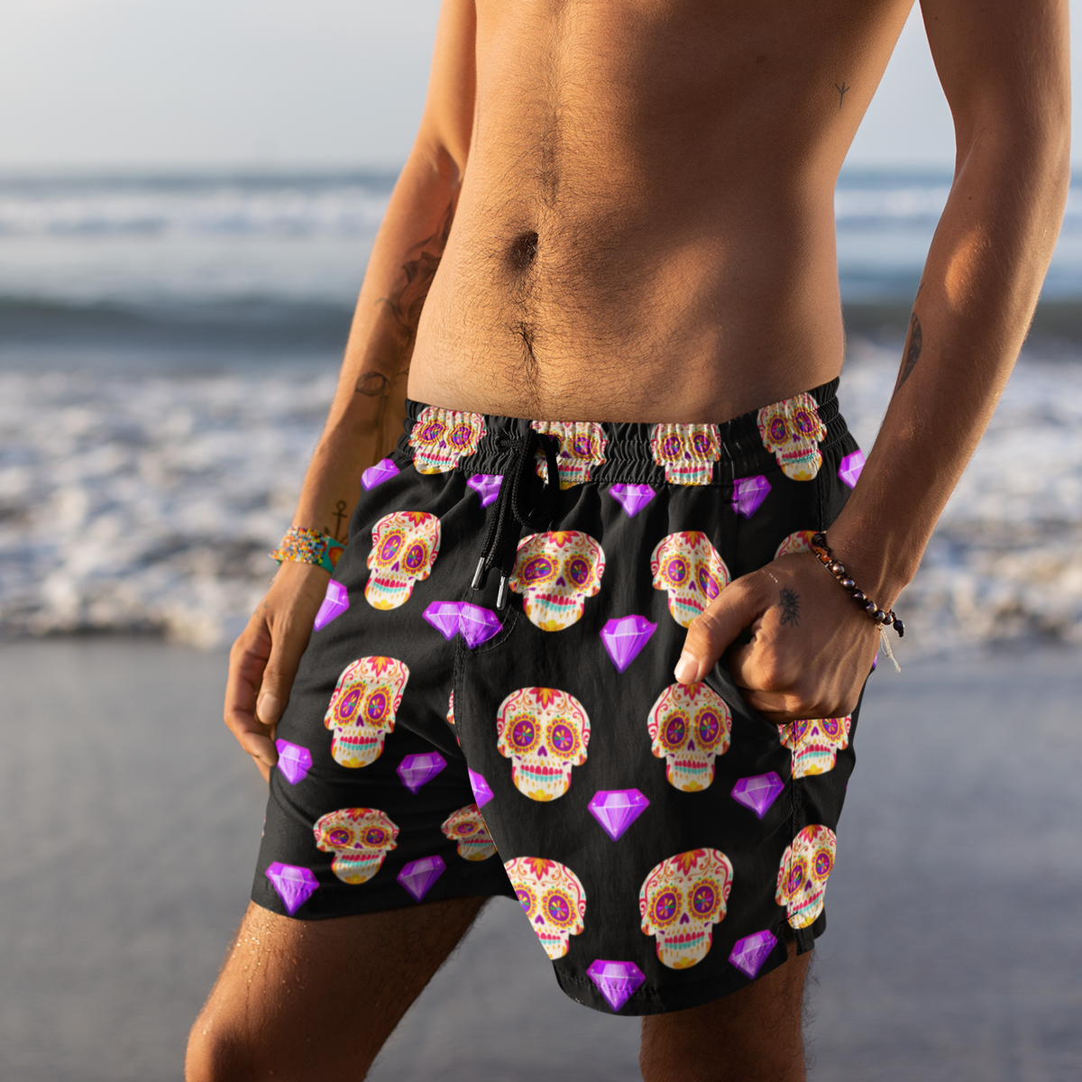Person wearing black swim shorts with colorful skull pattern on a beach.