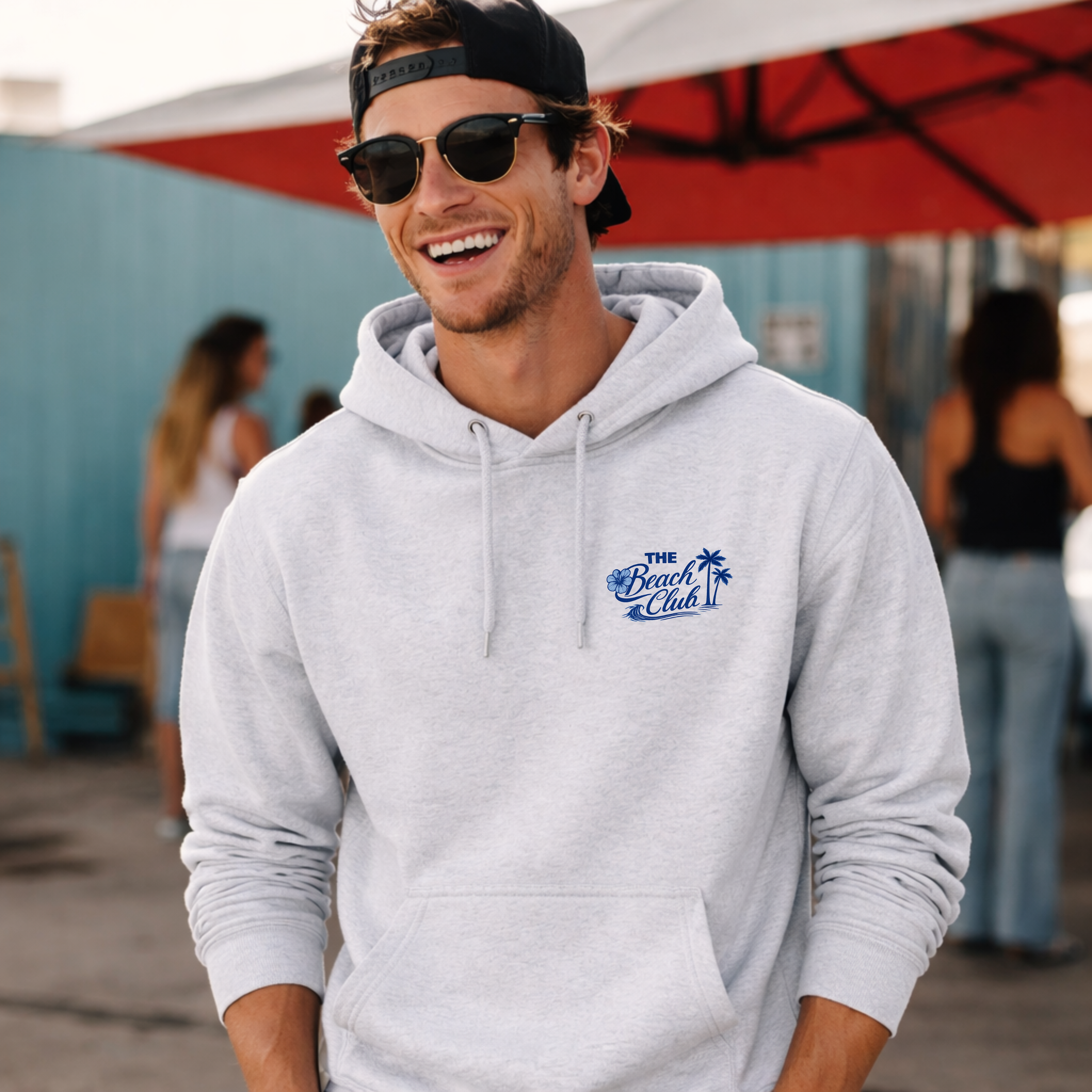 Man wearing a gray hoodie with 'The Beach Club' logo, smiling outdoors.